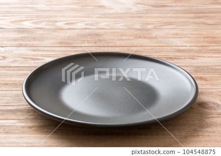 Perspective view of empty black plate on wooden background. Empty space for your design 104548875