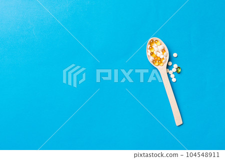 Vitamin capsules in a wooden spoon on a colored background. Pills served as a healthy meal. Drugs, pharmacy, medicine or medical healthycare concept 104548911