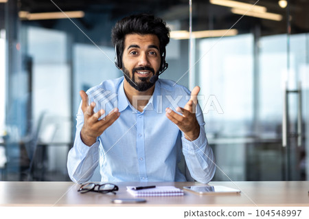 Webcam view, video call online meeting businessman smiling and talking friendly with colleagues clients, successful hispanic worker looking at camera working inside office with headset phone 104548997