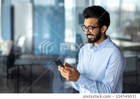Young successful mature businessman inside the office using the phone, man holding a smartphone online application user, smiling browsing the internet and dialing a call. 104549031
