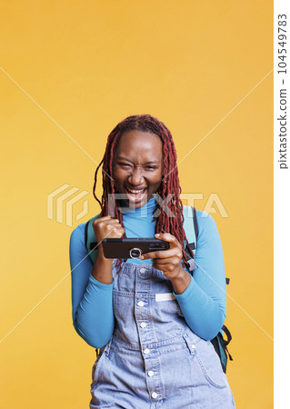 Joyful woman enjoying videogames win, playing mobile games online in studio. Female traveller having fun with shooter gaming challenge on smartphone app, journey trip destination. Joyful woman enjoying videogames win, playing mobile games online in studio. Female traveller having fun with shooter gaming challenge on smartphone app, journey trip destination. 104549783