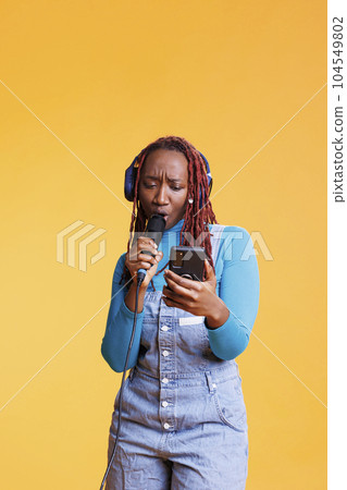 Woman creating sound performance live with microphone in studio, singing songs at musical party. Young musician talented artist having fun with karaoke, feeling confident with voice. 104549802