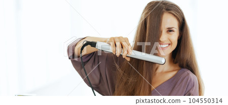 Happy young woman straightening hair in bathroom 104550314