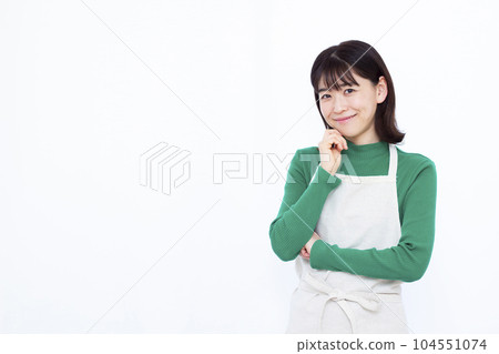 Housewife in her thirties wearing an apron thinking with a smile in front of a white background 104551074