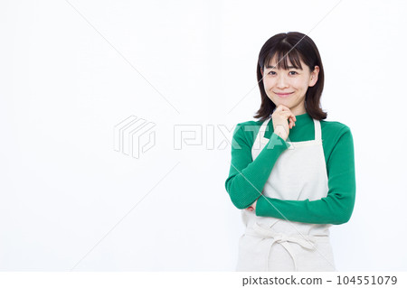 三十多歲的家庭主婦穿著圍裙，在白色背景前微笑著思考 104551079