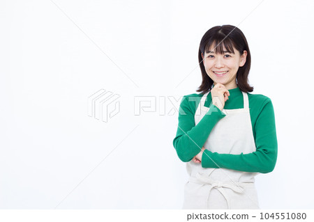 三十多歲的家庭主婦穿著圍裙,在白色背景前微笑著思考 三十多歲的家庭主婦穿著圍裙,在白色背景前微笑著思考 104551080