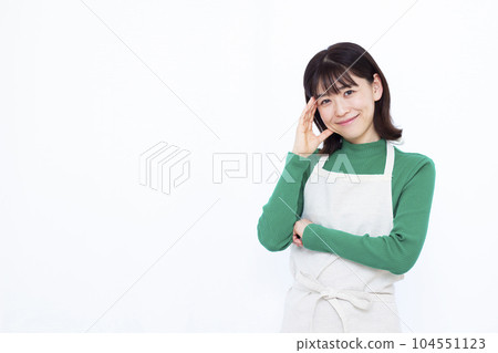 三十多歲的家庭主婦穿著圍裙，在白色背景前微笑著思考 104551123