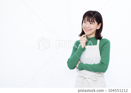 Housewife in her thirties wearing an apron thinking with a smile in front of a white background Housewife in her thirties wearing an apron thinking with a smile in front of a white background 104551212