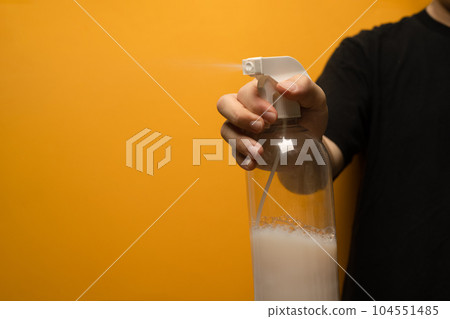 Hand holding plastic spray bottle isolated on yellow background. Domestic chores, cleanliness and hygiene concept Hand holding plastic spray bottle isolated on yellow background. Domestic chores, cleanliness and hygiene concept 104551485