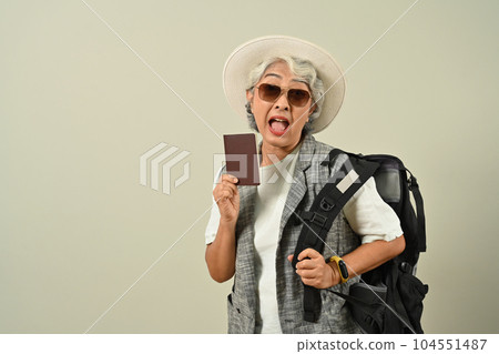 Smiling retired woman with backpack holding passport getting ready to travel on holidays on gray background 104551487