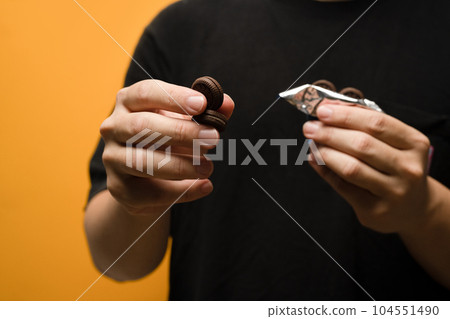 Unrecognizable man hand holding cookies with cream isolated on yellow background Unrecognizable man hand holding cookies with cream isolated on yellow background 104551490