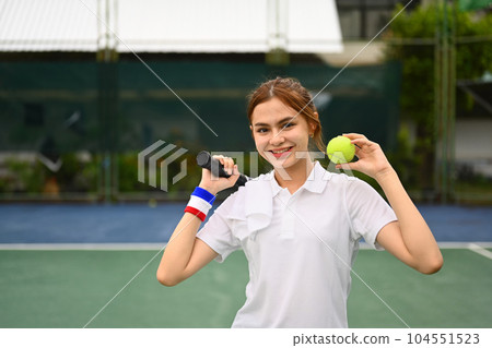 Cheerful sportswoman holding racket and ball standing on the tennis court. Fitness, sport and competition concept 104551523