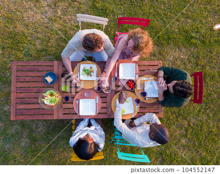 Multi ethnic group of young friends eating together outdoors on summer garden party. Aerial view of Multi ethnic group of young friends eating together outdoors on summer garden party. Aerial view of 104552147