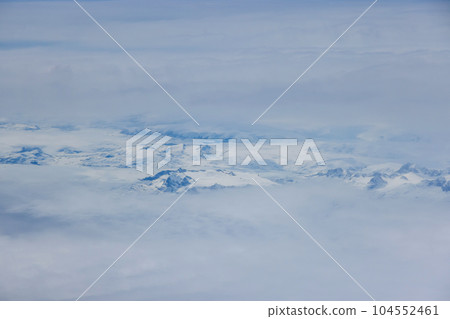 Amidst clouds majestic Greenland mountain peaks emerge adorned with blanket of glistening snow Amidst clouds majestic Greenland mountain peaks emerge adorned with blanket of glistening snow 104552461