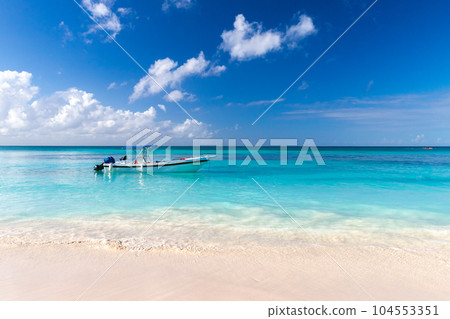 Coastal Caribbean landscape with fishing boat anchored near empty sandy beach 104553351