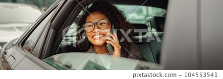 Smiling woman talking by phone with friends while sitting on back seat in taxi on way to work 104553541
