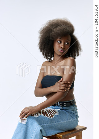 Portrait of beautiful, young, african woman with curly hair posing in top and jeans against white studio background 104553914