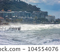 Rough waves crashing into the coast with various buildings situated nearby on the shore 104554076