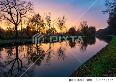 Serenity's Canvas: Dramatic Sunset Sky with Tree Silhouettes Reflected in River Serenity's Canvas: Dramatic Sunset Sky with Tree Silhouettes Reflected in River 104554376