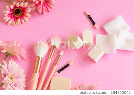 粉色背景上排列的化妝刷、粉撲和海綿等化妝工具 104555042