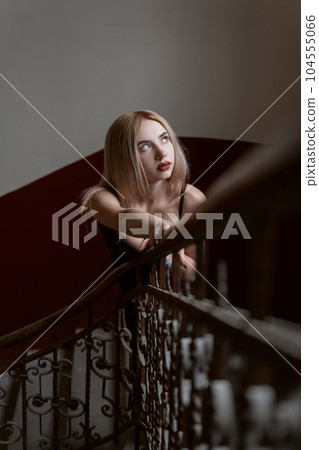 Beautiful young sad woman near stairs looking up. Model poses for photo indoor. Dark photo 104555066