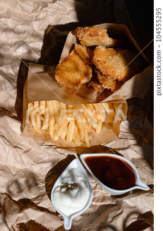 Chicken nuggets with sauce and french fries on a sheet of paper. 104555295