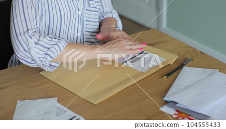 Close up female hands putting letter in envelop return form. Woman sends a return form by letter. Close up female hands putting letter in envelop return form. Woman sends a return form by letter. 104555433