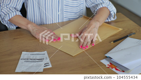 Close up female hands putting letter in envelop return form. Woman sends a return form by letter. Close up female hands putting letter in envelop return form. Woman sends a return form by letter. 104555434