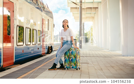 Young pretty woman sitting on her luggage and waiting train departure. Station is in background. Concept of vacation and business trip Young pretty woman sitting on her luggage and waiting train departure. Station is in background. Concept of vacation and business trip 104556238