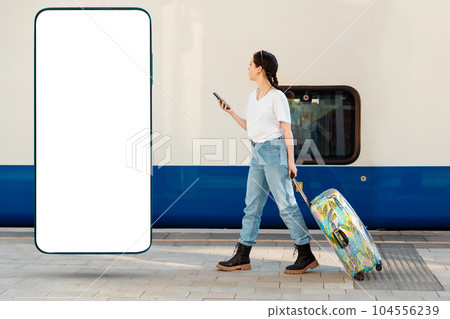 Side view of young woman walking with her luggage using cellphone. Tarin in background. Big smartphone with mock up and copy space. Concept of travel and business trip. Side view of young woman walking with her luggage using cellphone. Tarin in background. Big smartphone with mock up and copy space. Concept of travel and business trip. 104556239