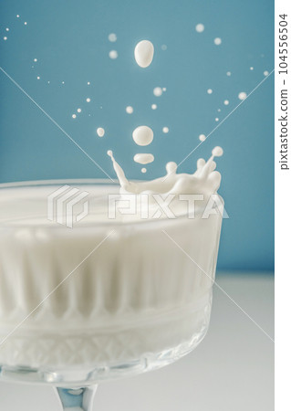 Milk pours into a beautiful crystal glass on a blue background and splashes around. 104556504