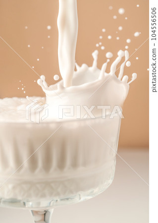 Milk pours into a beautiful crystal glass and splashes around. Milk pours into a beautiful crystal glass and splashes around. 104556506