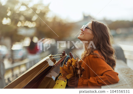 happy trendy woman in brown trench coat with shopping bags 104556531