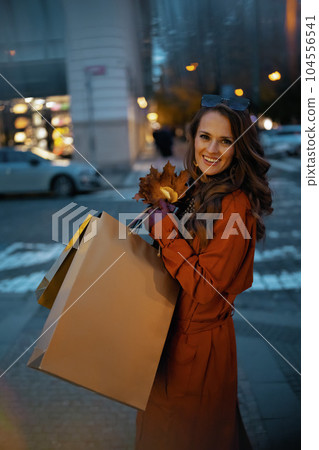 smiling trendy female in brown trench coat with shopping bags smiling trendy female in brown trench coat with shopping bags 104556541
