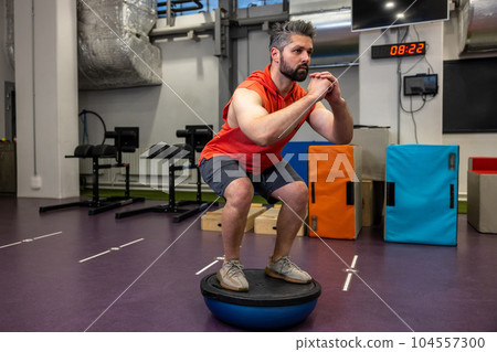 Fit athletic man performing exercise on gymnastic hemisphere bosu ball in gym. Fit athletic man performing exercise on gymnastic hemisphere bosu ball in gym. 104557300