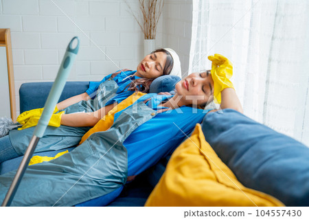 Two Asian housekeeper or housemaid women lie and sleep on sofa after feel tired from cleaning house Two Asian housekeeper or housemaid women lie and sleep on sofa after feel tired from cleaning house 104557430