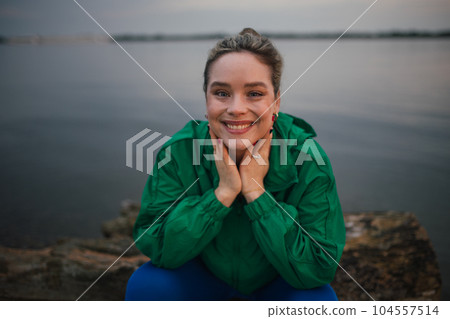 Portrait of happy woman in sportive clothes resting near lake. Portrait of happy woman in sportive clothes resting near lake. 104557514