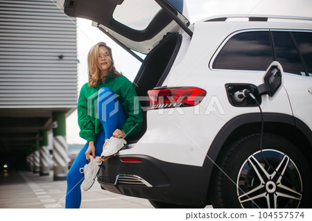 Young woman in sportive clothes waiting for her electric car charging. Young woman in sportive clothes waiting for her electric car charging. 104557574