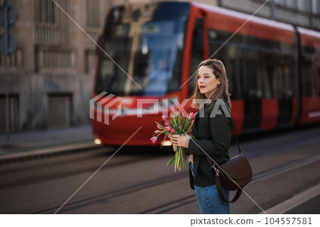 Portrait of young woman in city with bouquet of tulips. 104557581