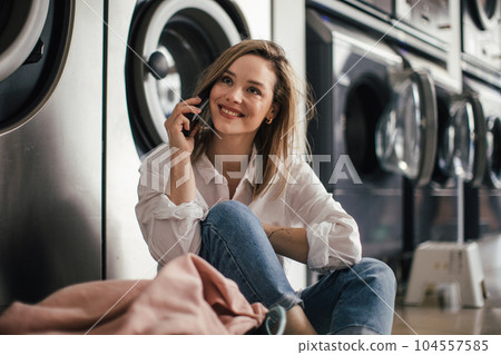 Young woman calling, waiting in a laundry room. Young woman calling, waiting in a laundry room. 104557585