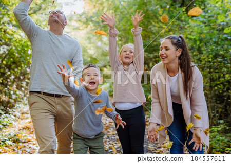 Happy family having fun with a foliage in autumn forest. 104557611