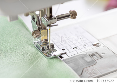 Modern sewing machine presser foot with green fabric and thread, closeup, macro 104557922