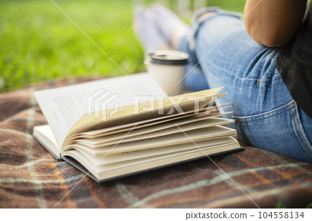 A woman in jeans with a book and a cup of coffee sits on a blanket in the park A woman in jeans with a book and a cup of coffee sits on a blanket in the park 104558134