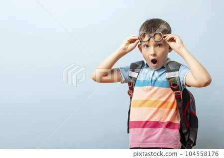Surprised schoolboy in glasses with backpack on blue background. Back to school Surprised schoolboy in glasses with backpack on blue background. Back to school 104558176