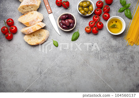 Food composition with sliced ciabatta, olives, olive oil, spaghetti, fresh basil, cherry tomatoes on gray concrete stone rustic background top view, space for text. Italian cuisine concept Food composition with sliced ciabatta, olives, olive oil, spaghetti, fresh basil, cherry tomatoes on gray concrete stone rustic background top view, space for text. Italian cuisine concept 104560137