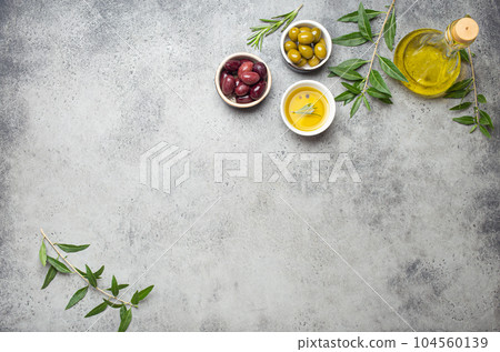 Composition with green and brown olives, extra virgin olive oil in glass bottle, olive tree branches on gray concrete stone rustic background top view, copy space border 104560139