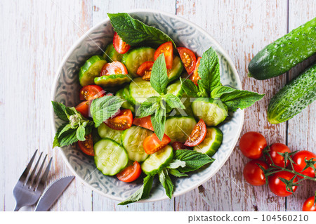 Close up of salad of cucumbers, cherry tomatoes and mint leaves in a bowl on the table top view Close up of salad of cucumbers, cherry tomatoes and mint leaves in a bowl on the table top view 104560210