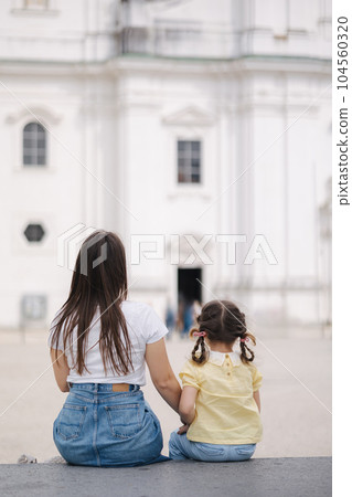 Back view of little girl sits with her mom on stone bench outdoor 104560320