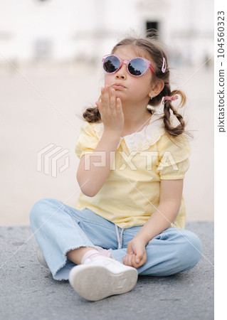 Portrait of adorable little girls sits on stone bench. Happy girl in sunglasses Portrait of adorable little girls sits on stone bench. Happy girl in sunglasses 104560323