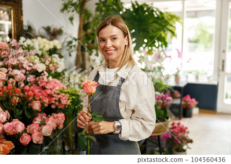 Smiling woman florist hold rose ready to sell on floral background and looking at camera 104560436
